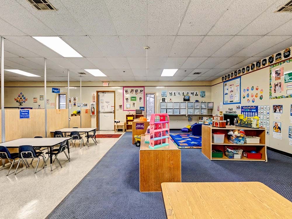 Classroom with tables, chairs, and play areas with toys and shelves