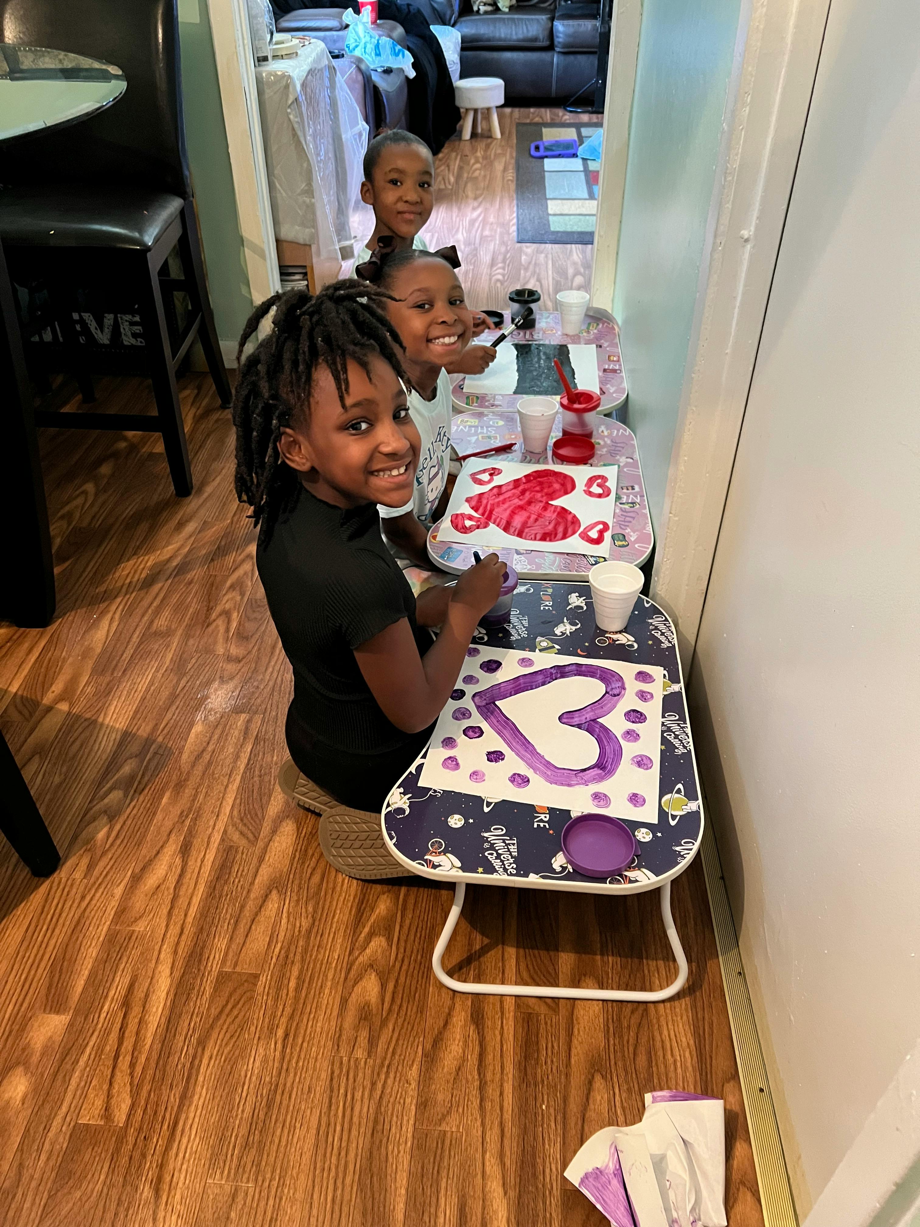 Three children painting hearts at small tables
