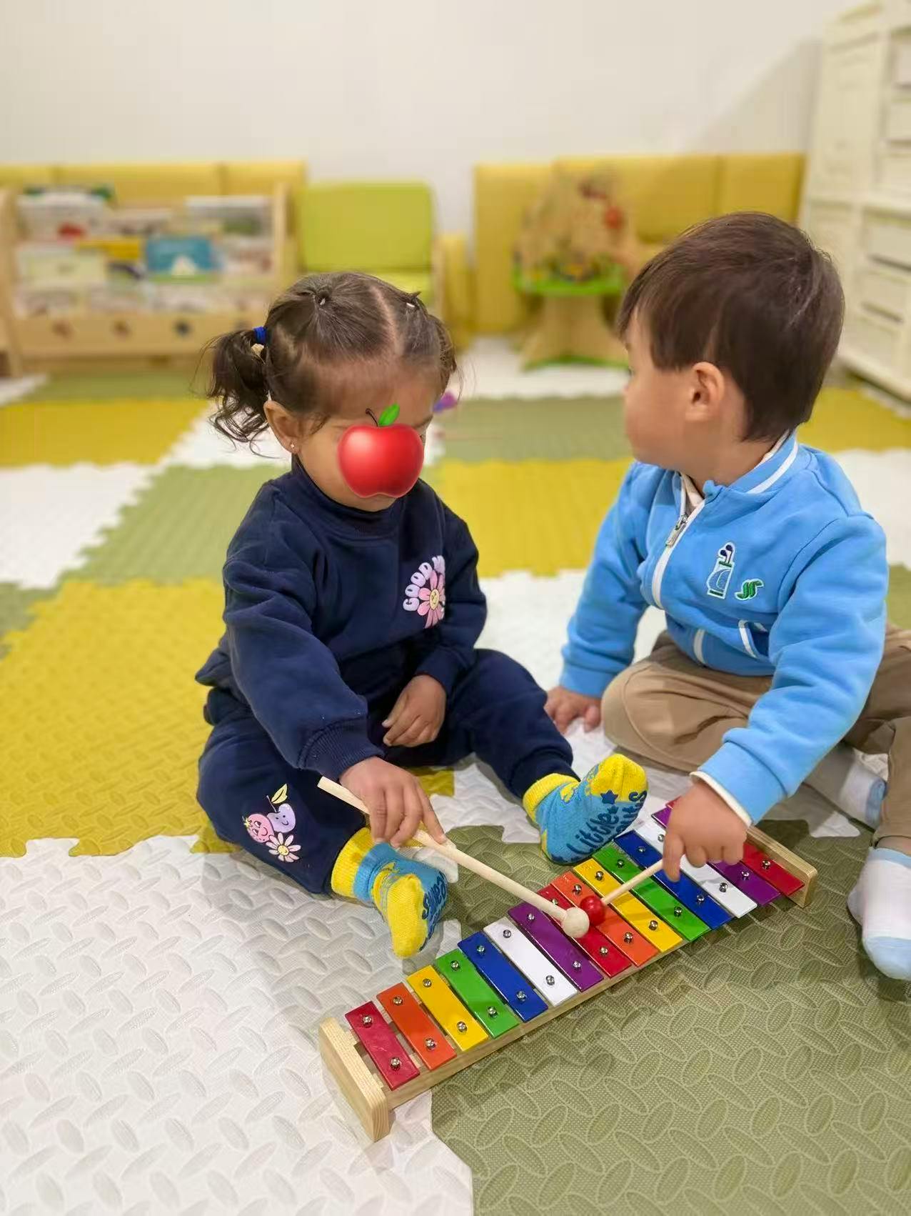 Two children sitting on a mat playing with a colorful xylophone
