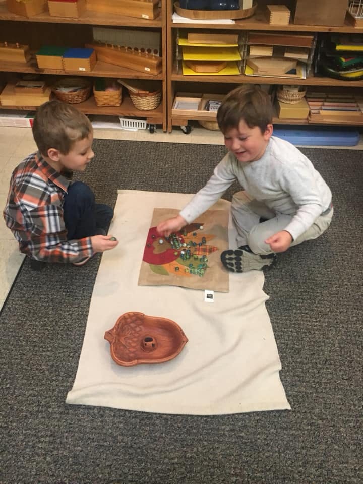 Two children sitting on the floor, one playing with a craft