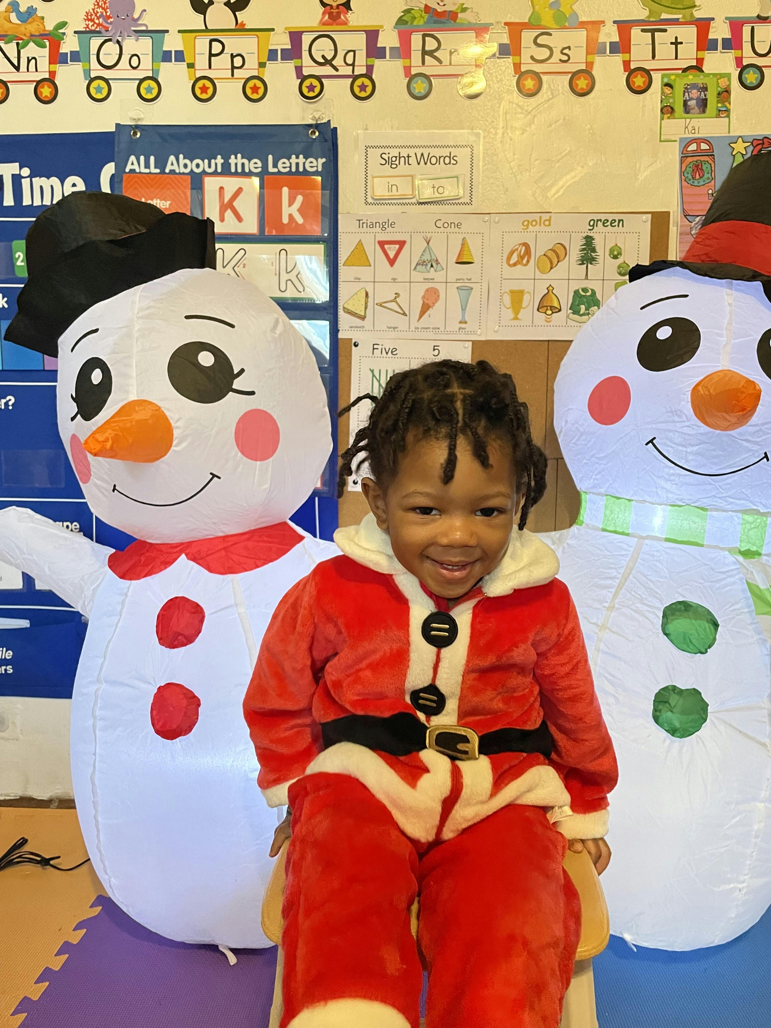 Child in Santa costume sitting between two snowman decorations