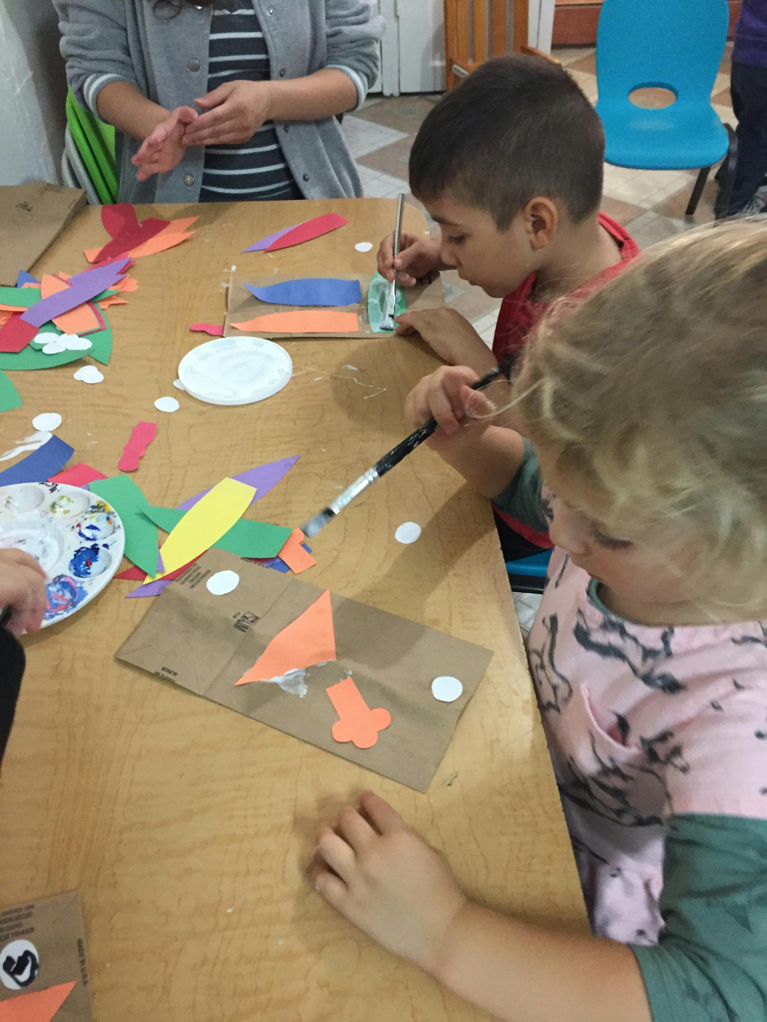 Two children painting and gluing paper shapes at a table