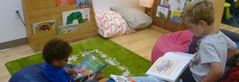 Two children reading books on a green rug