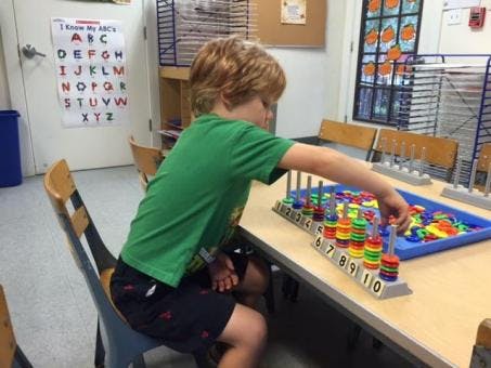 Child playing with colorful counting rings at a table in a classroom