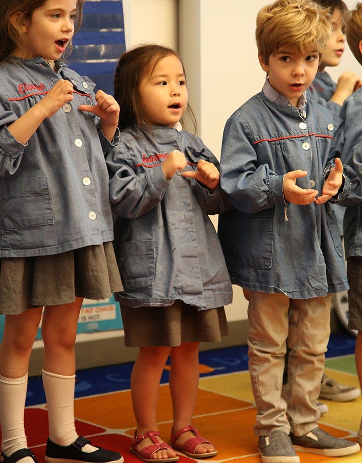 Three children in uniform with open mouths and hands gesturing