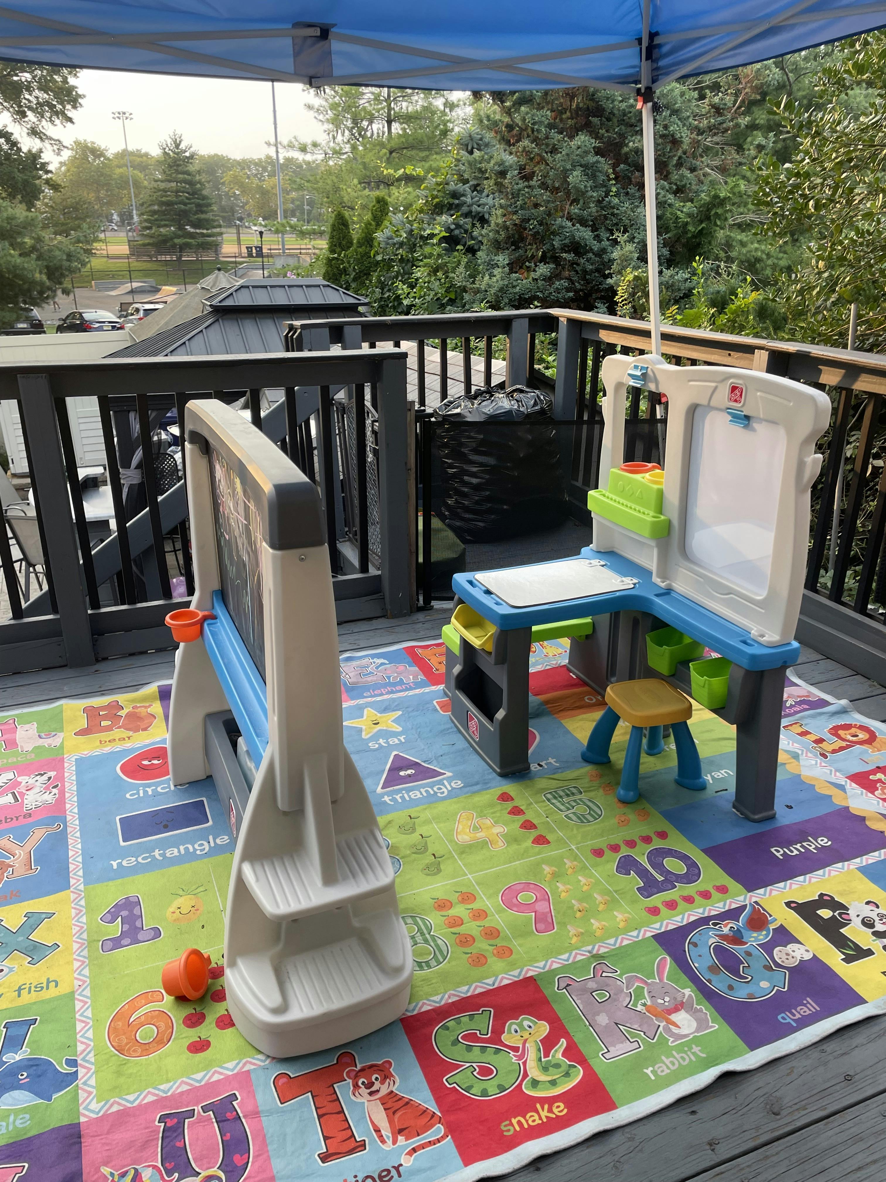 Children's art easel and desk on a colorful alphabet rug outdoors