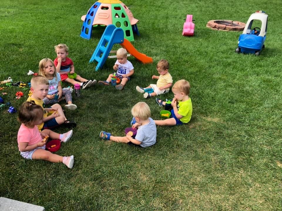 Children sitting on grass with toys and playground equipment