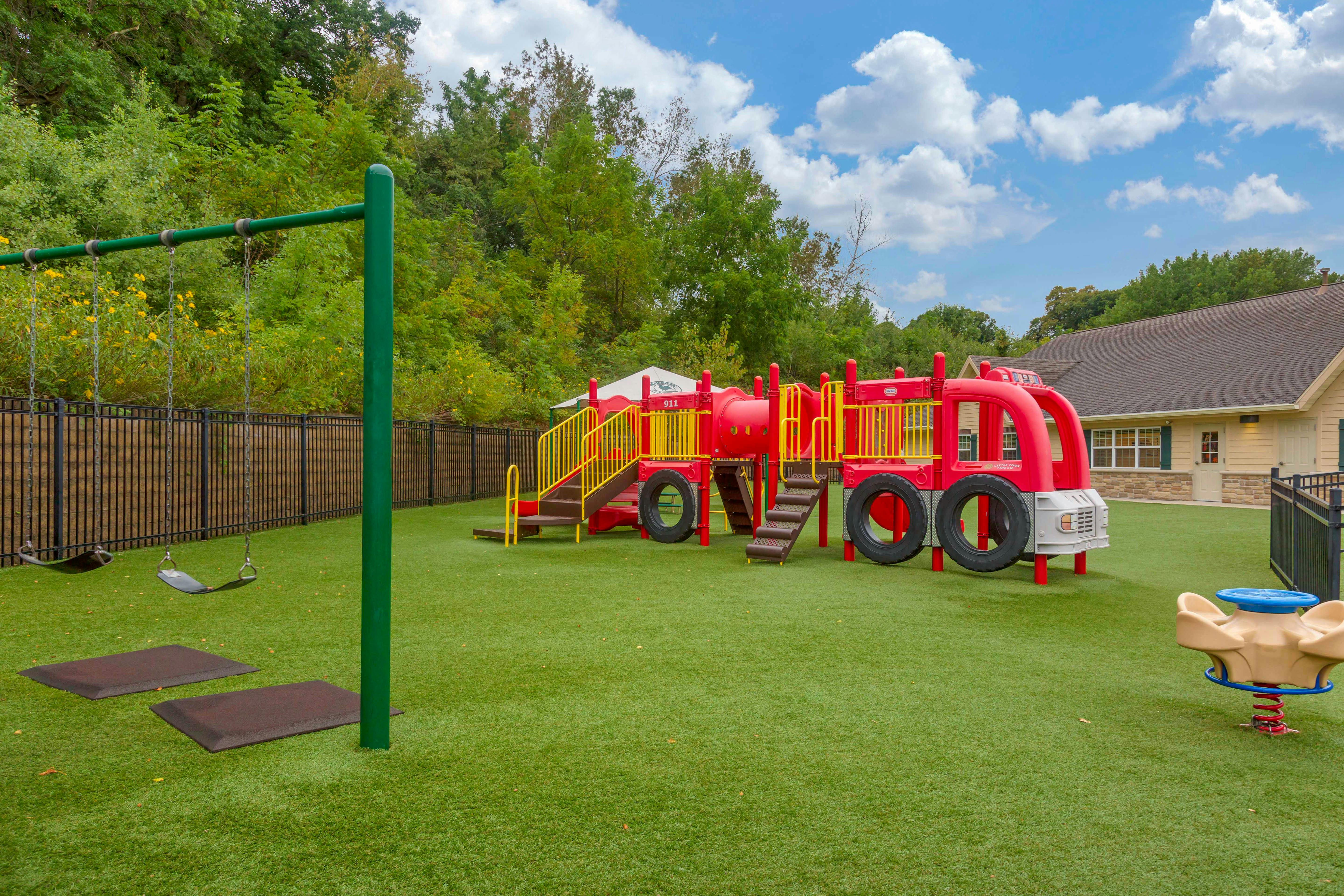 Playground with green turf, a red fire truck play structure, and swings