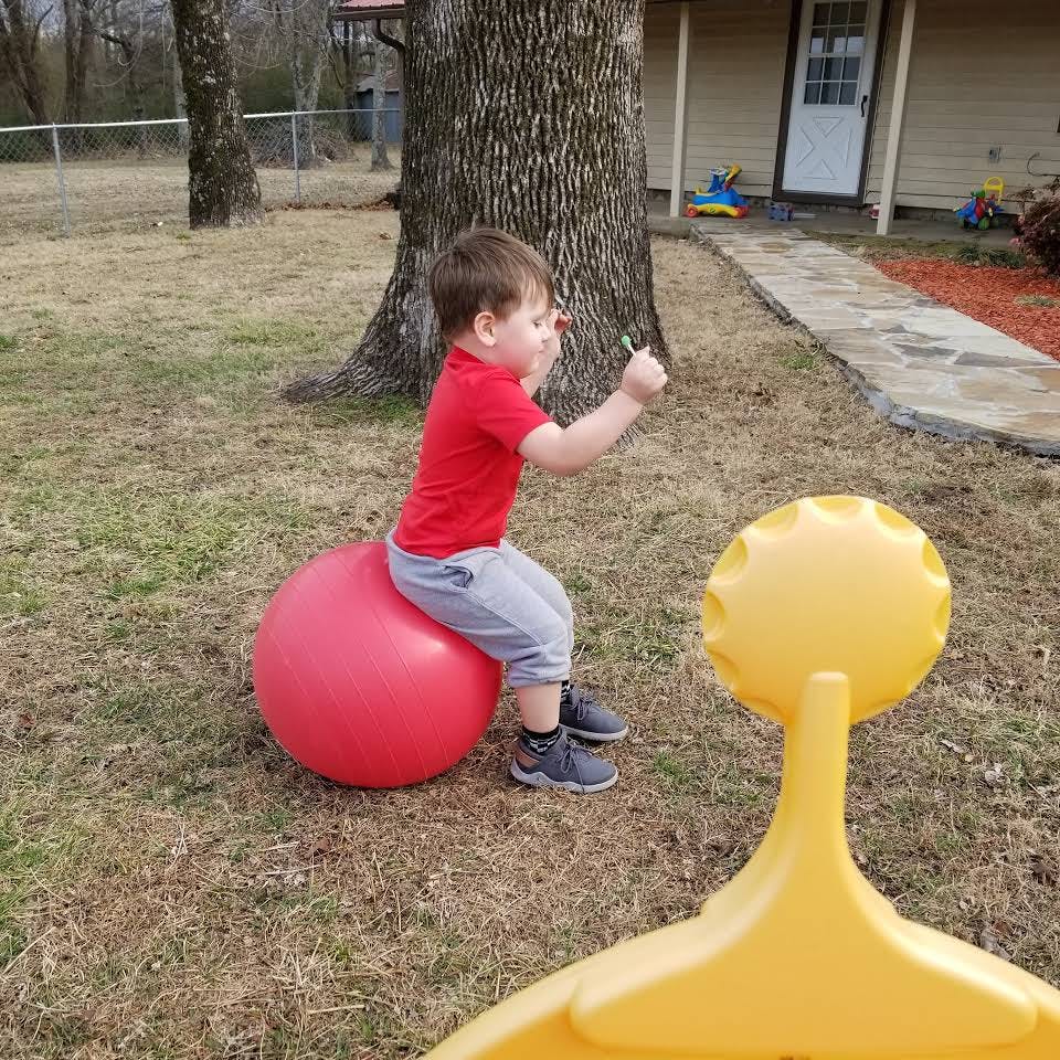Child sitting on a red exercise ball outdoors