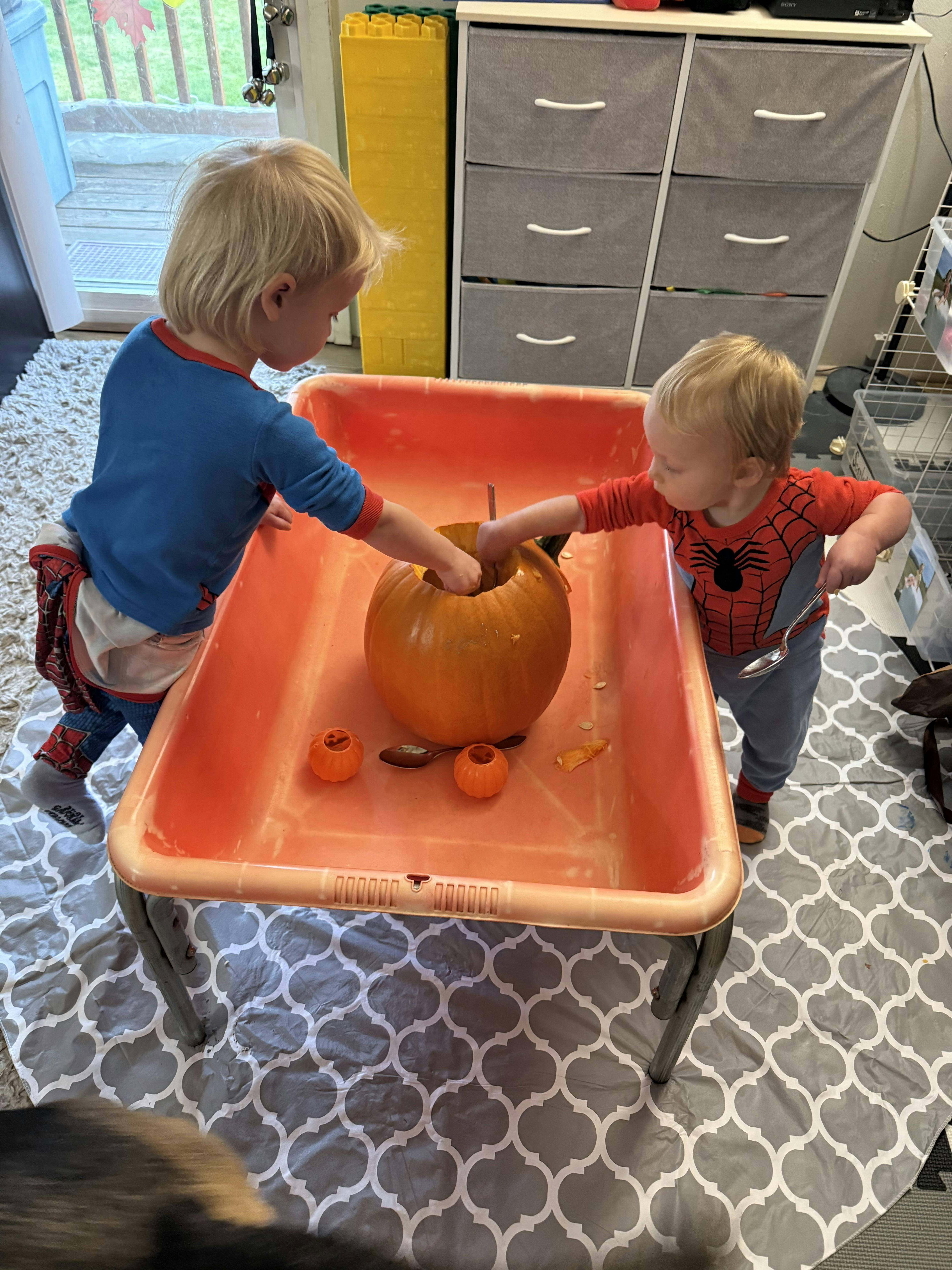 Two children carving a pumpkin in a plastic bin
