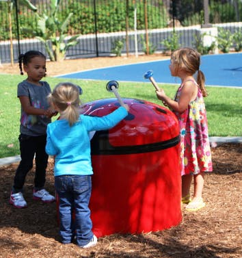 Three children playing with a large red drum in a playground