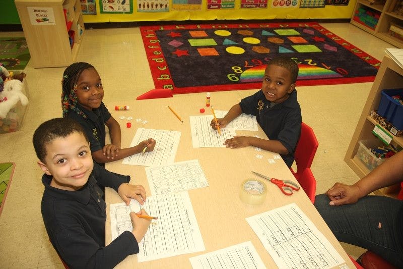 Three children writing at a table in a classroom