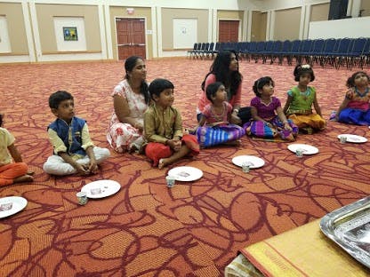 Adults and children sitting on a patterned carpet with plates