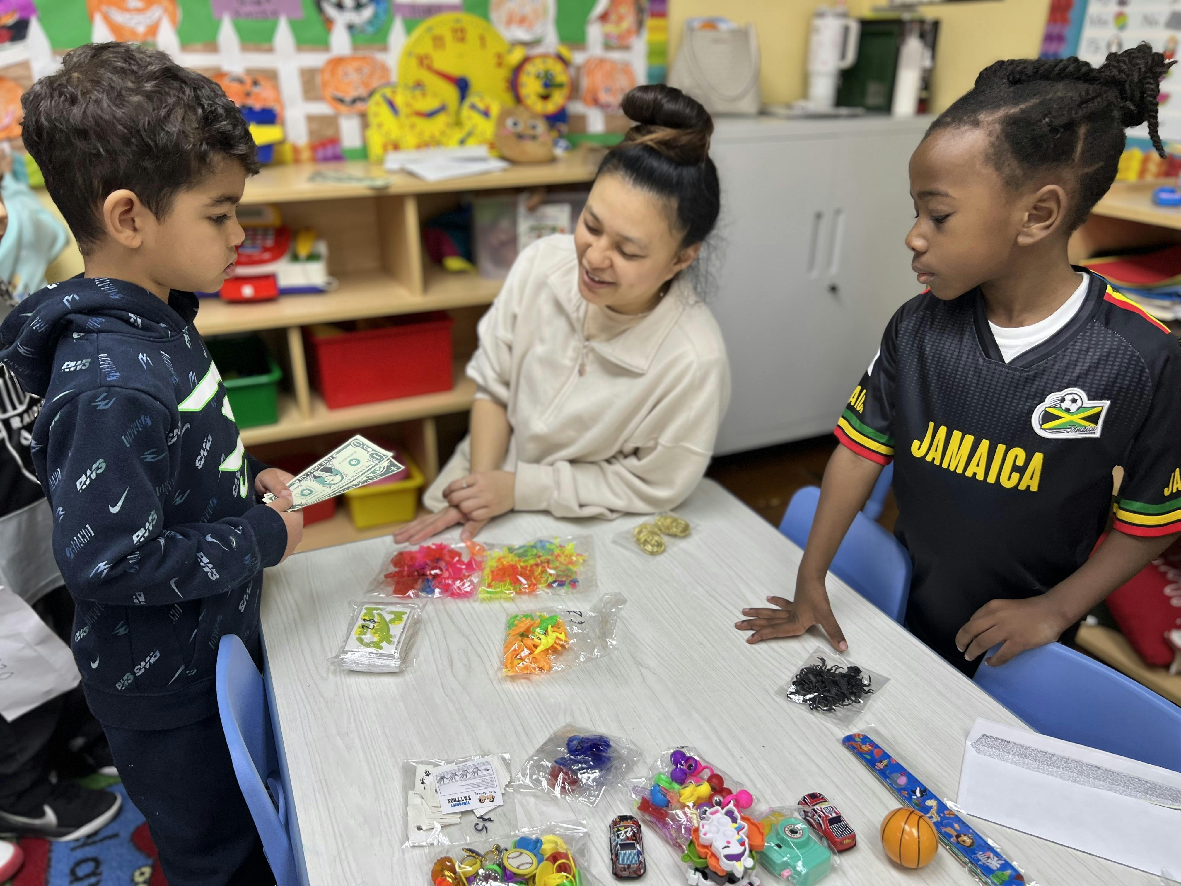 Adult and two children at a table with small toys and money