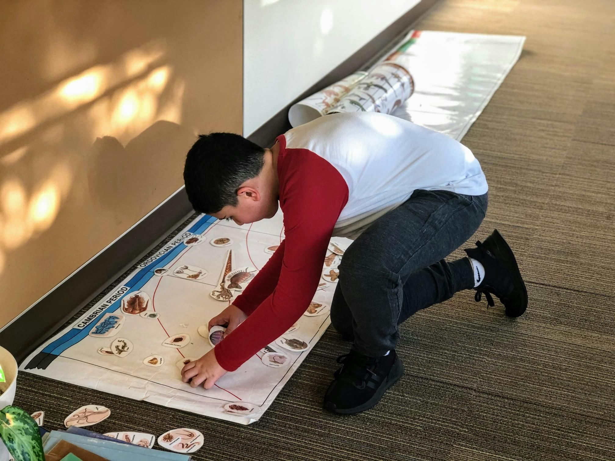 Child kneeling on floor, playing with items on a long paper