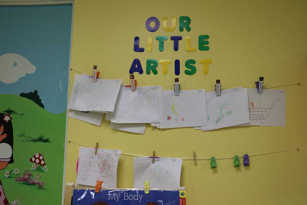 Children's drawings displayed on a wall with "OUR LITTLE ARTIST" text