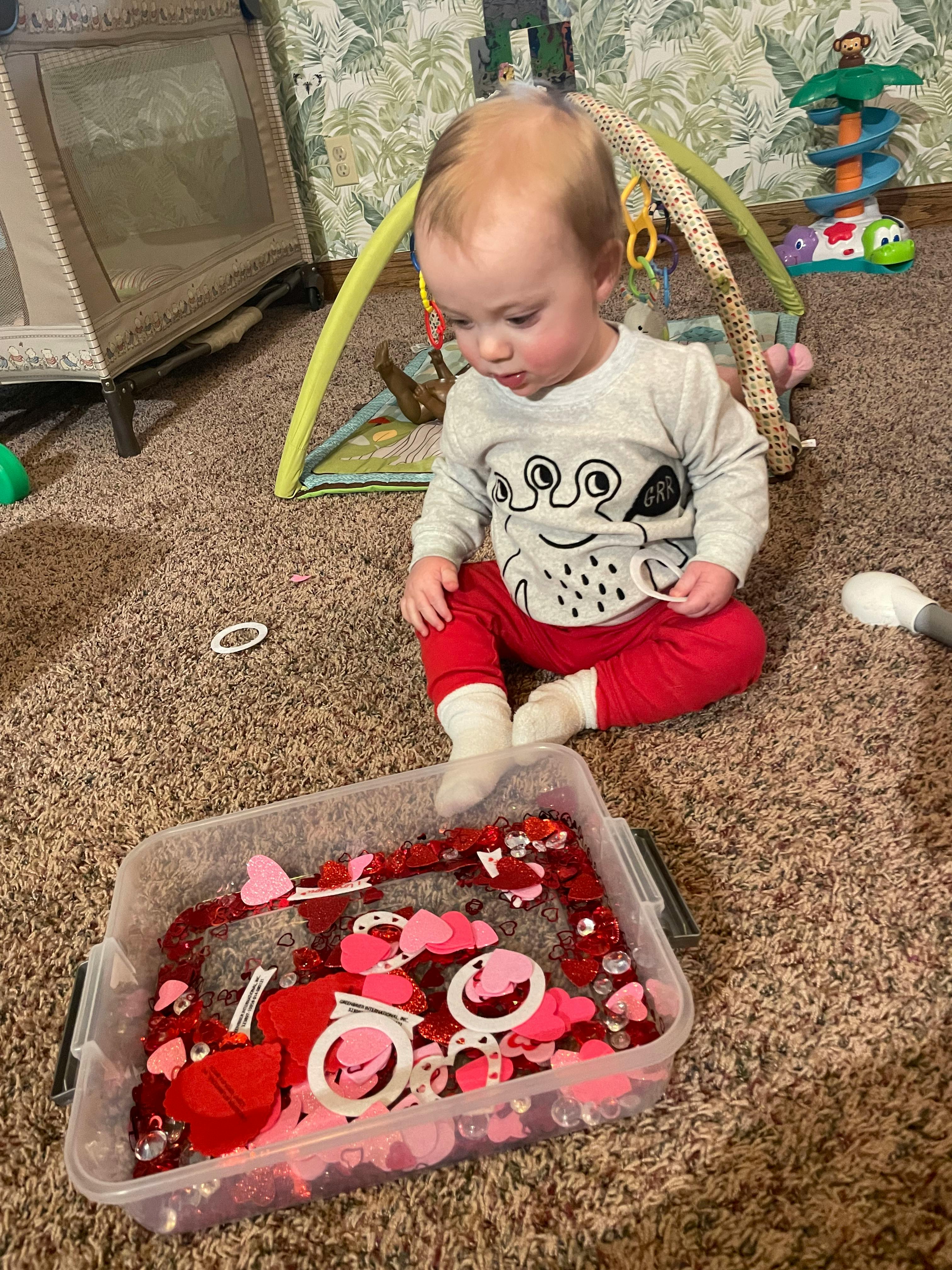 Child sitting on carpet looking at a container of red and pink craft items