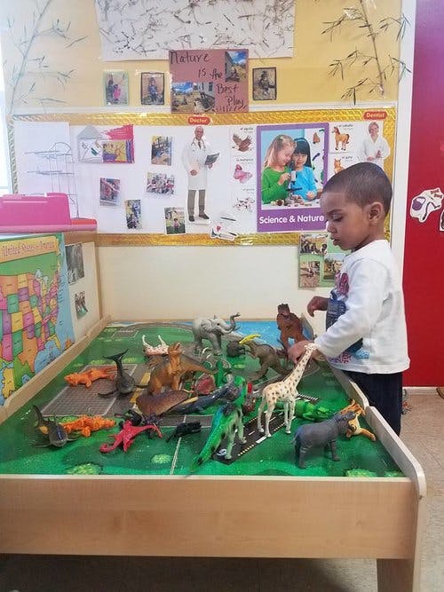 Child playing with animal figurines on a green play table