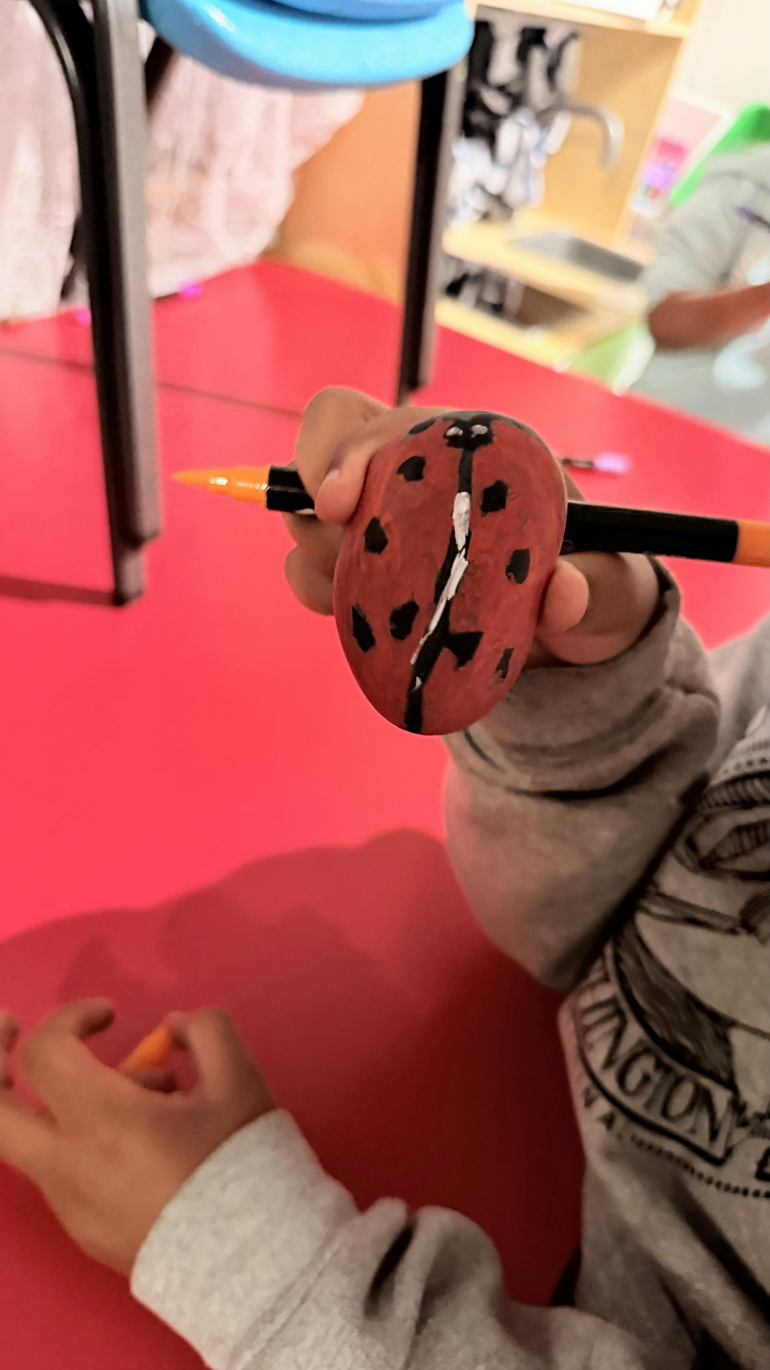 Child holding a ladybug-painted rock and marker