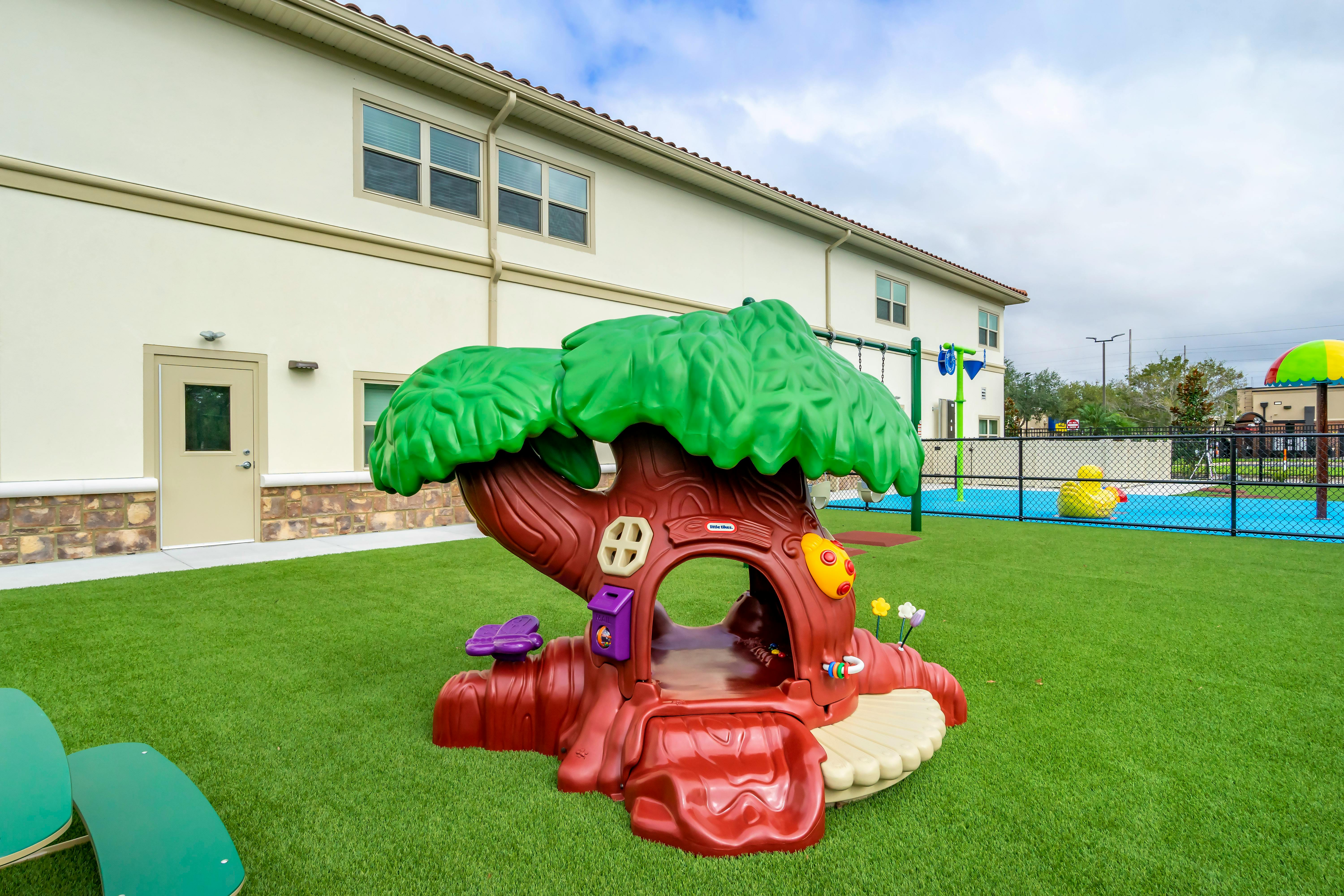 A children's playground with a tree-shaped climbing structure on artificial grass