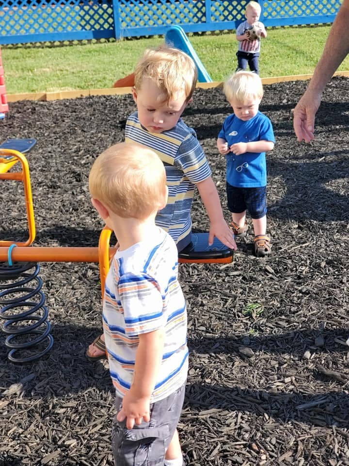 Three children playing on a playground with wood chips