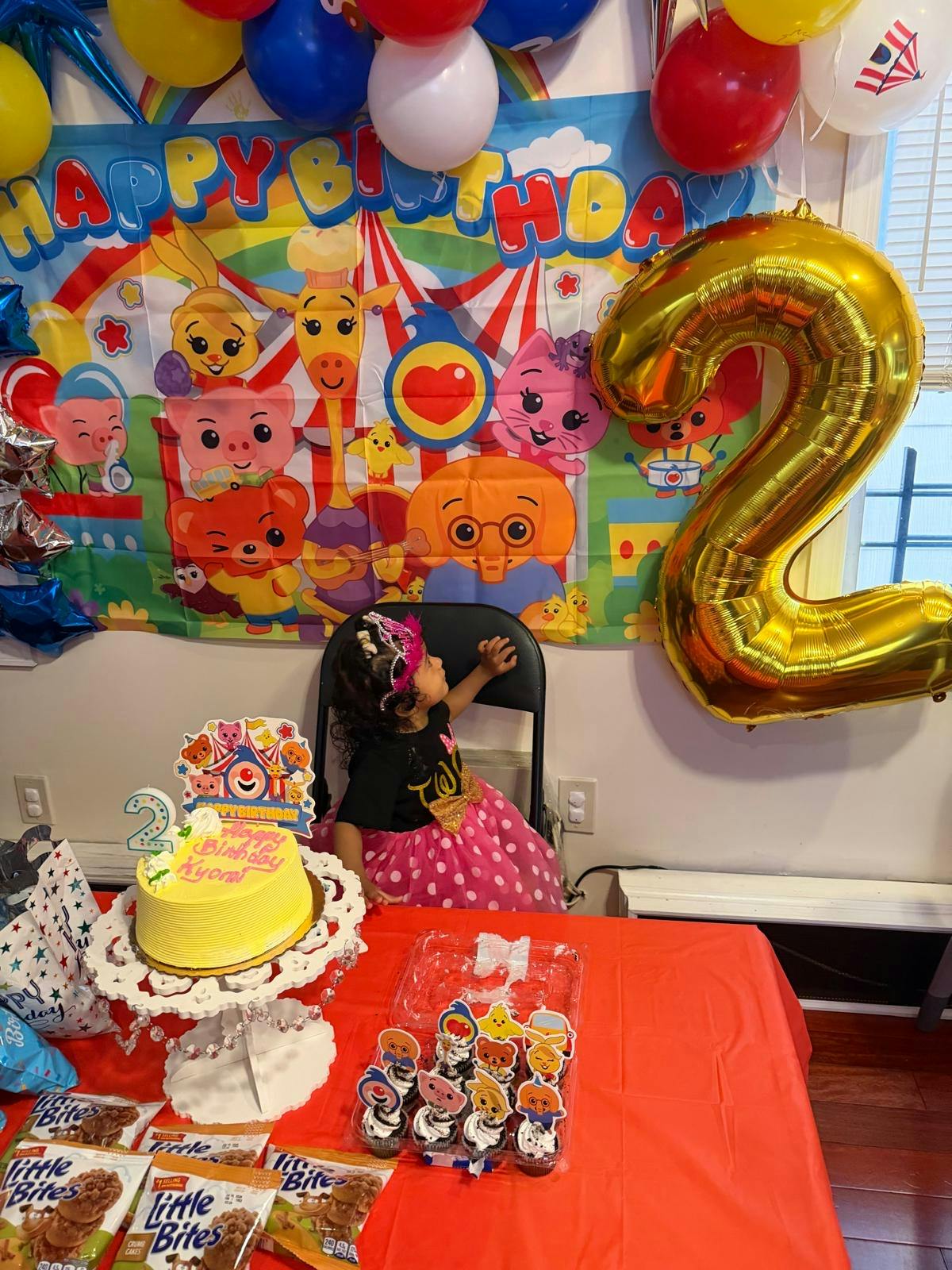 Child wearing a crown sitting at a birthday party with a number two balloon