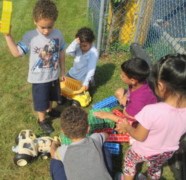 Children playing with toy trucks and blocks outdoors