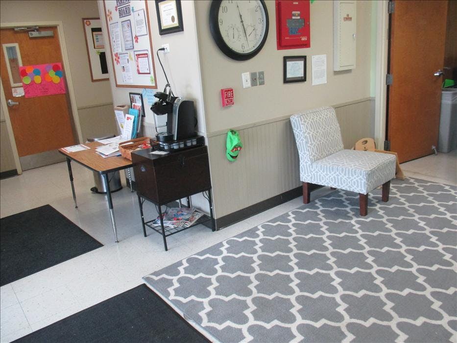 An empty waiting area with a coffee maker, table, chair, and patterned rug