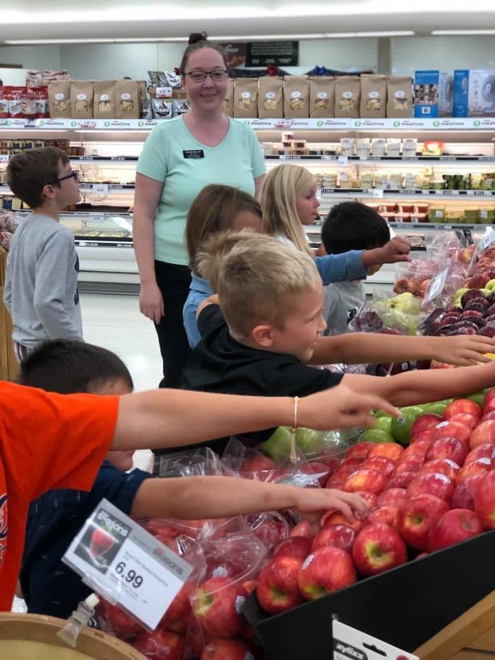 Adult and children reaching for apples in a grocery store
