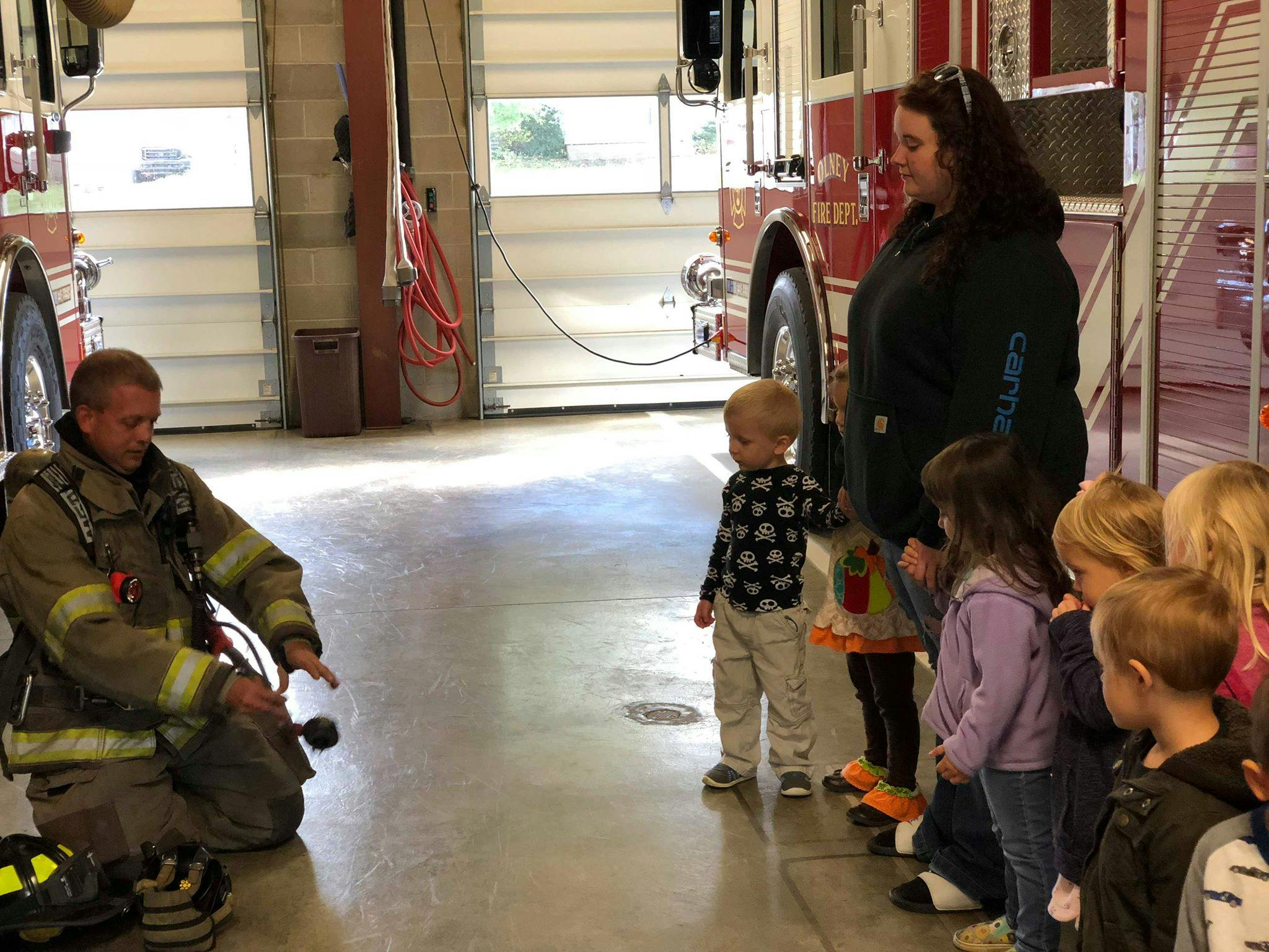 Firefighter kneeling in front of children and an adult in a fire station