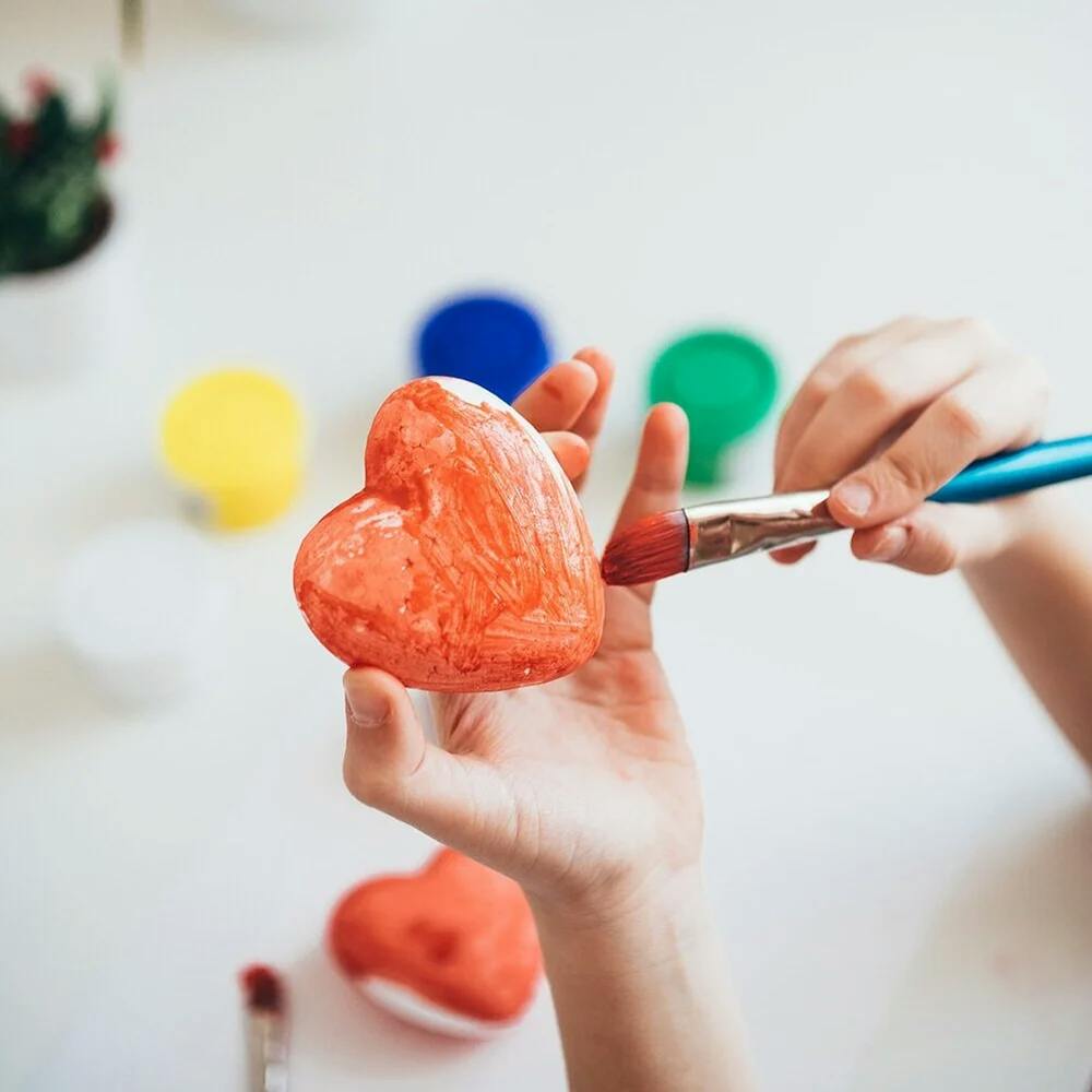 Child's hands painting a heart shape with a paintbrush
