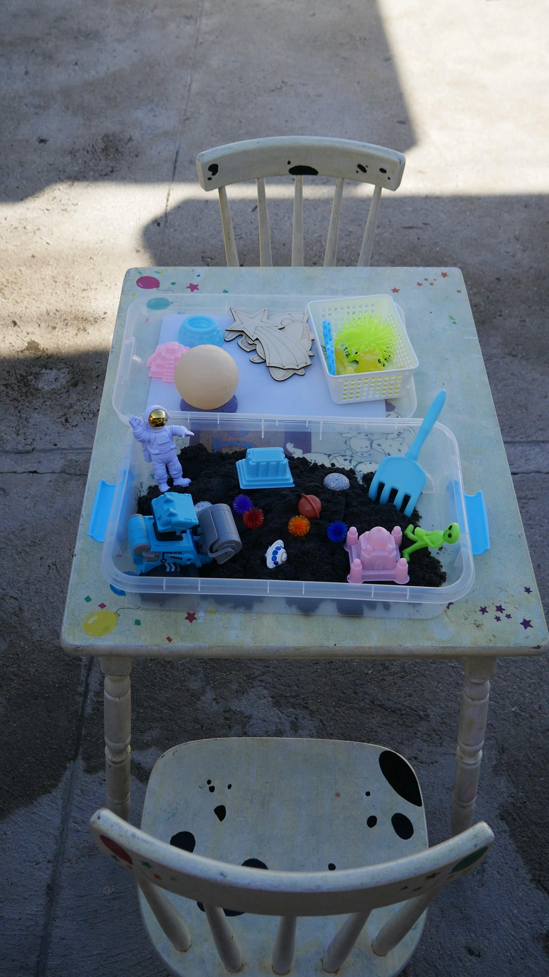 Table with a sensory bin filled with toys and dark material