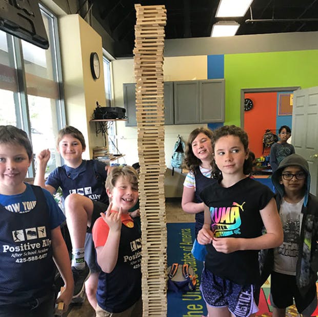 Children standing around a tall wooden block tower
