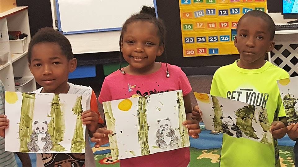 Three children holding up drawings of pandas and bamboo
