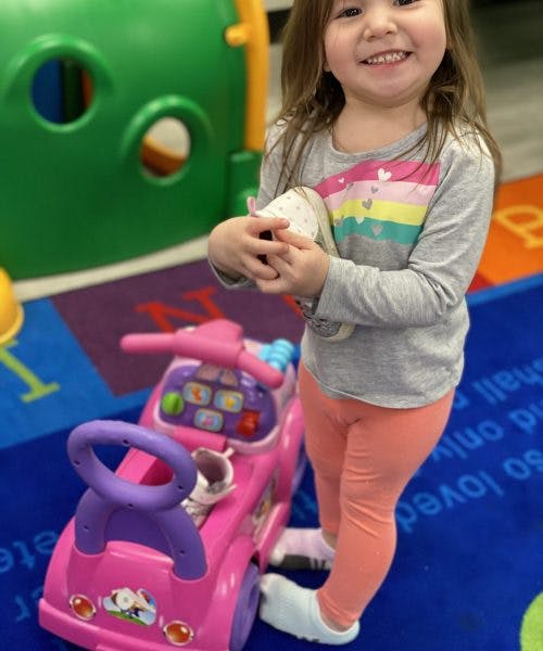 Child standing next to a pink toy car