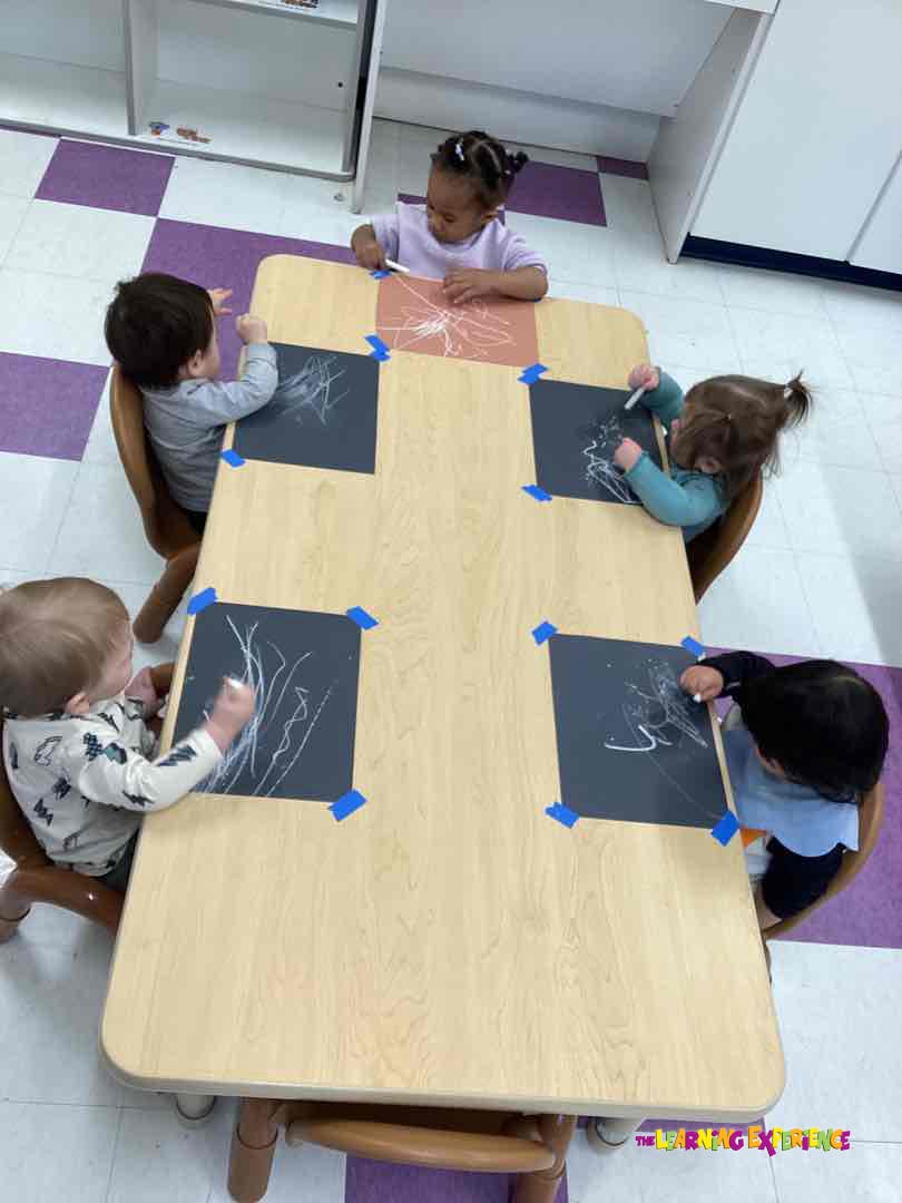Five children drawing with chalk at a table