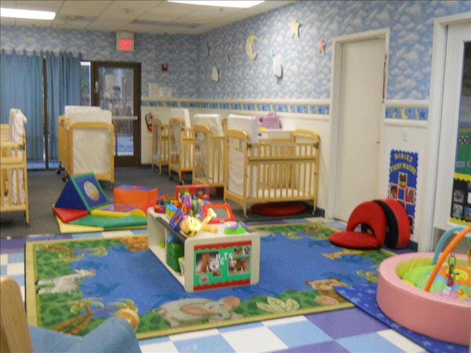 A colorful nursery room with multiple cribs, a play rug, and various toys