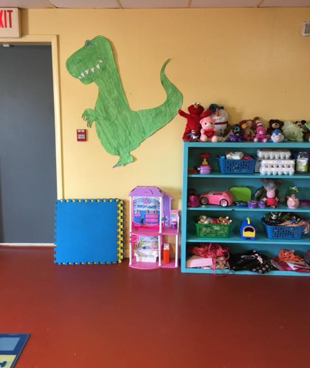 Playroom with a green dinosaur cutout on the wall and shelves of toys