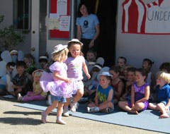 Two children dancing in front of other children sitting on the ground