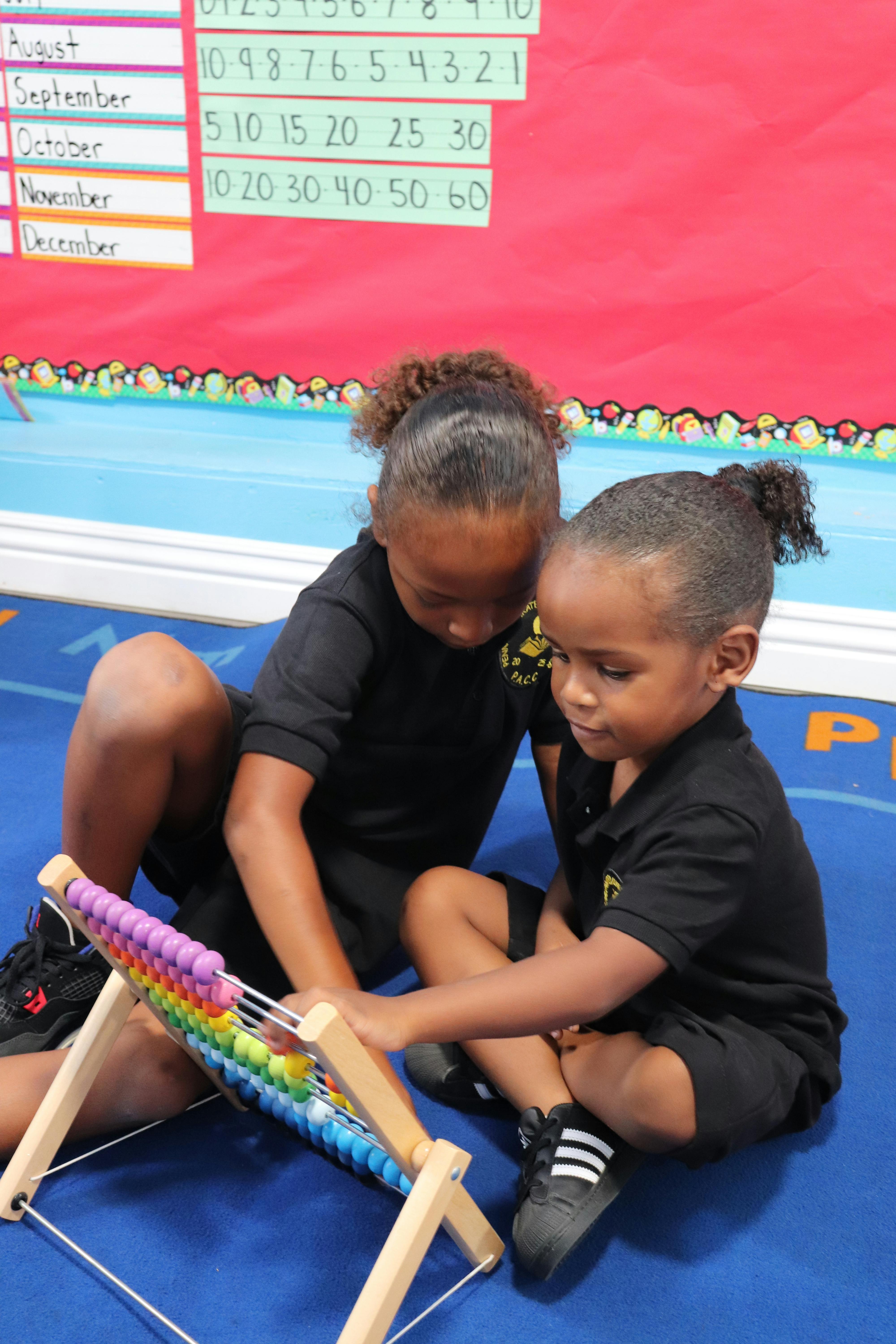 Two children on a blue floor looking at a colorful abacus