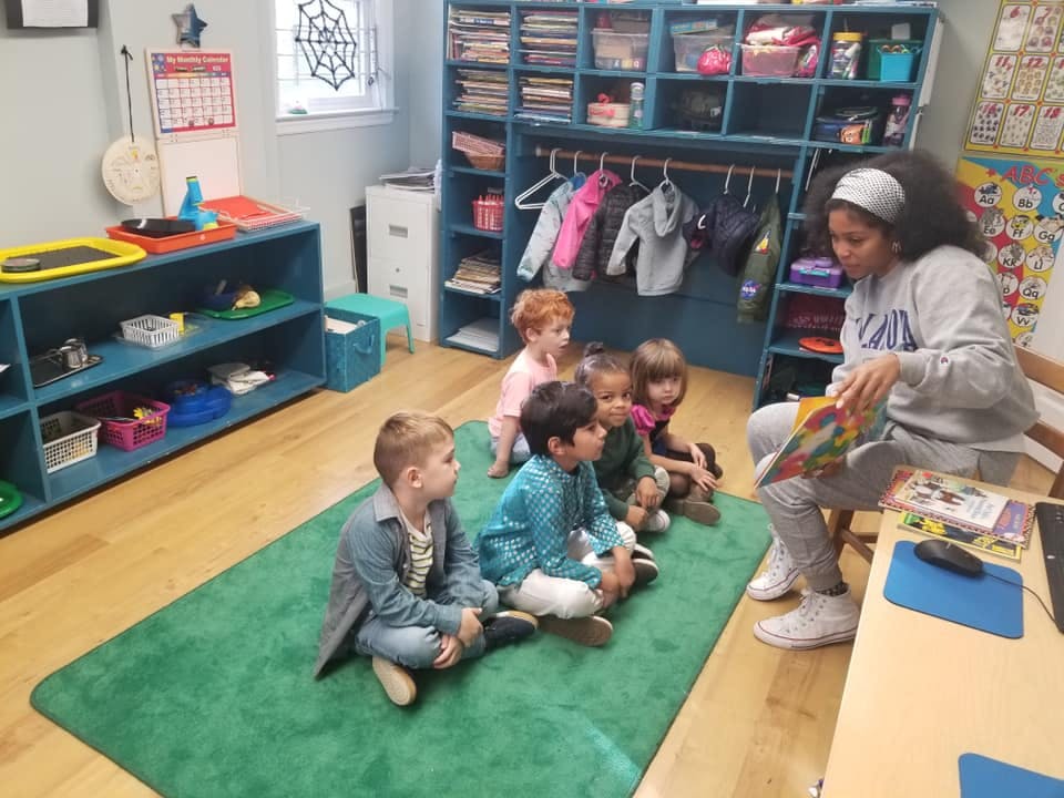 Adult reading a book to children sitting on a rug in a classroom
