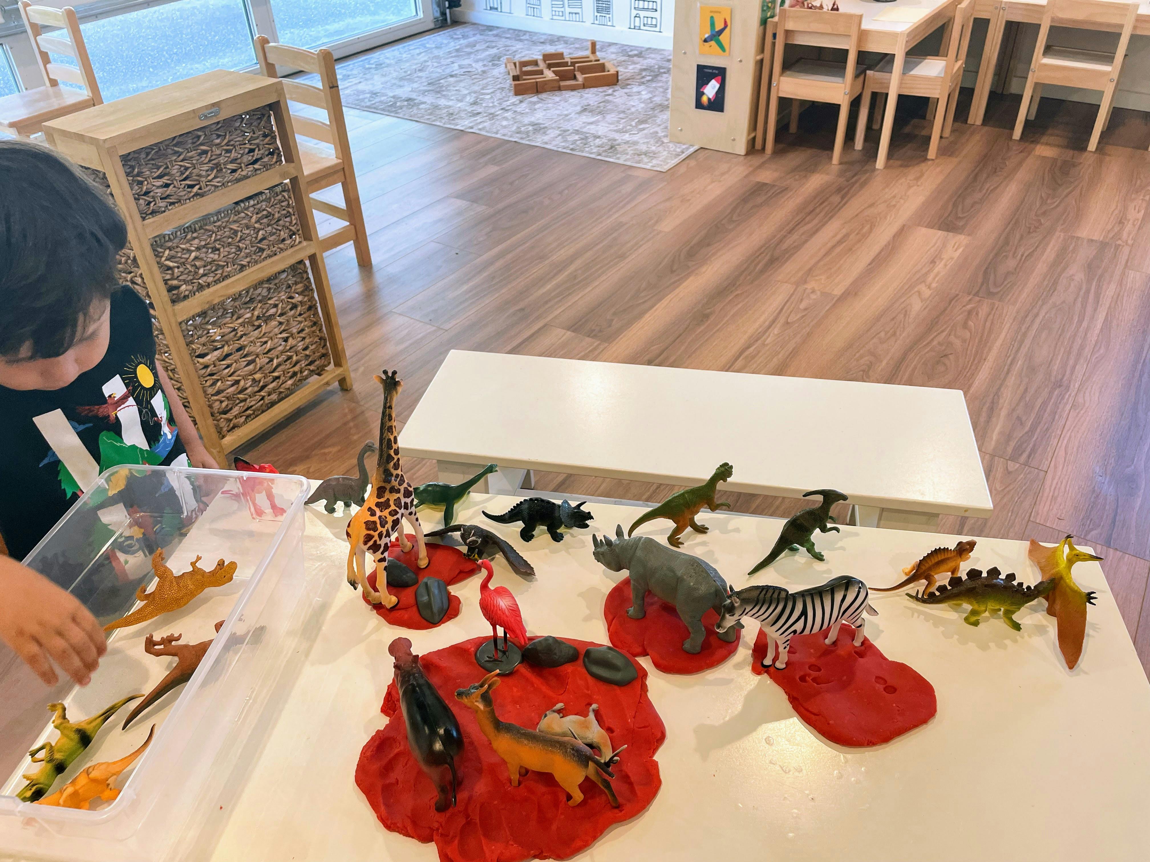 Child playing with animal figurines on red playdough in a classroom