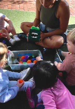 Person and children playing with a green monster toy and colorful pom-poms