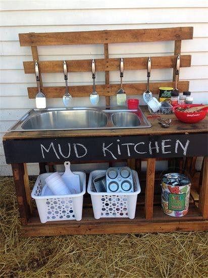 Outdoor mud kitchen with two sinks and kitchen utensils hanging above