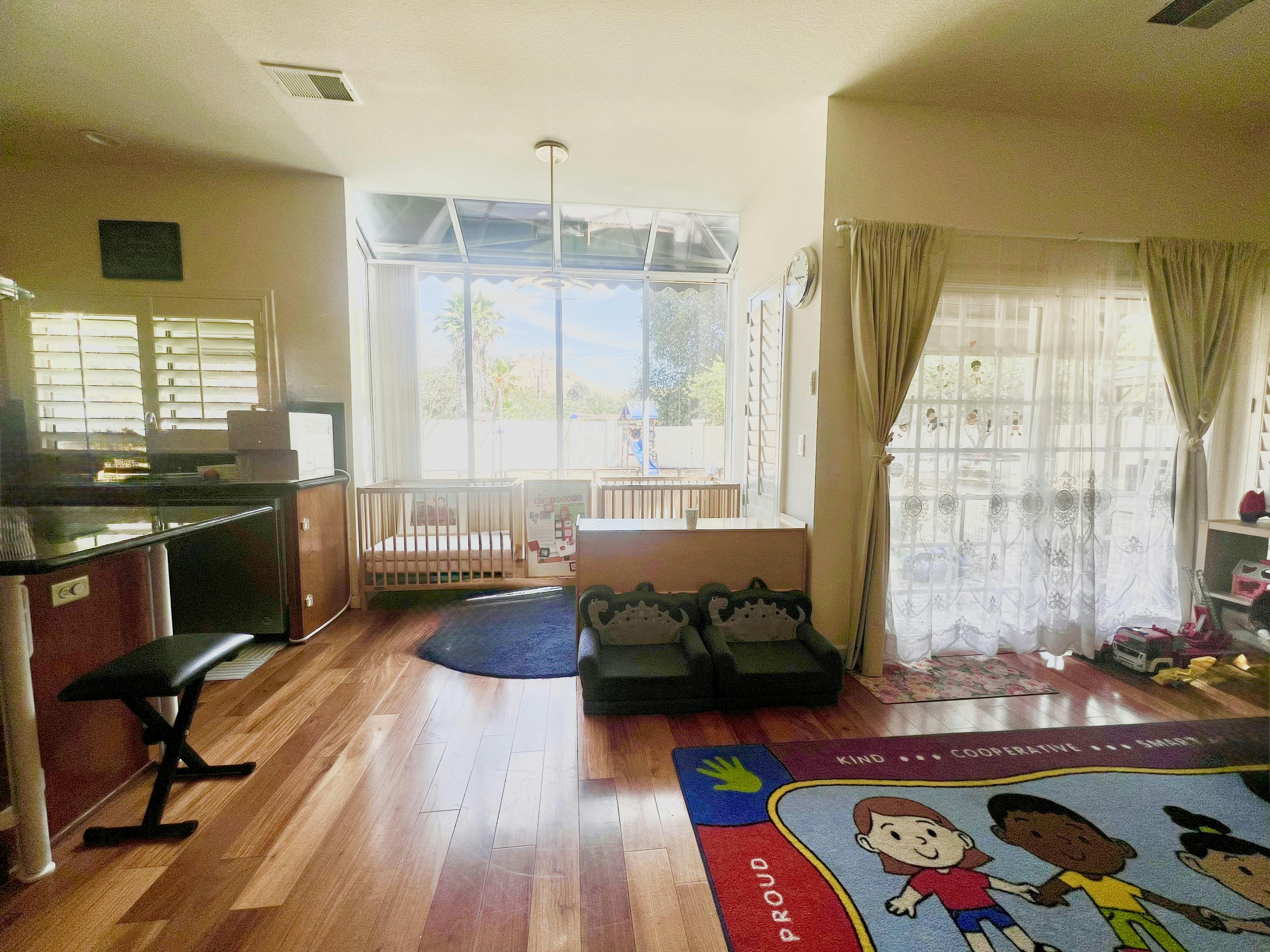 Playroom with two cribs, small chairs, and a colorful rug with cartoon children