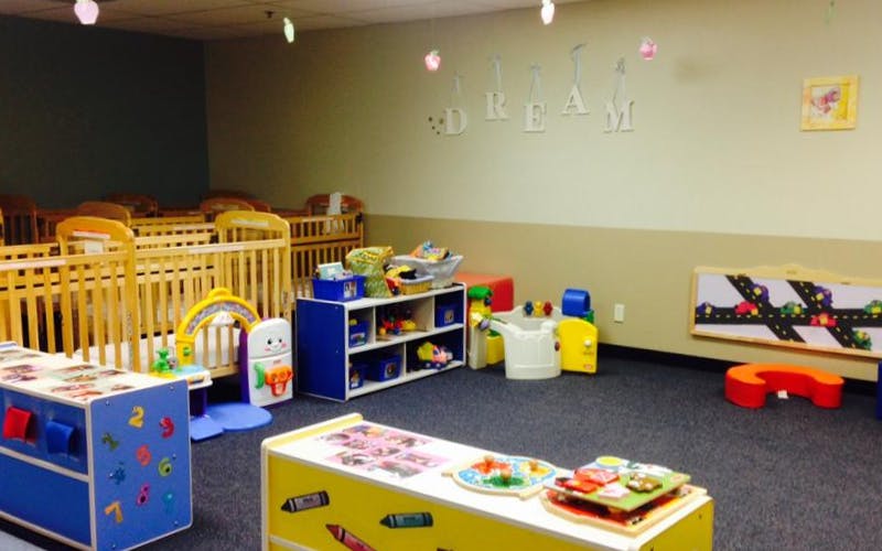cribs in a daycare room with toys and a \"DREAM\" sign on the wall