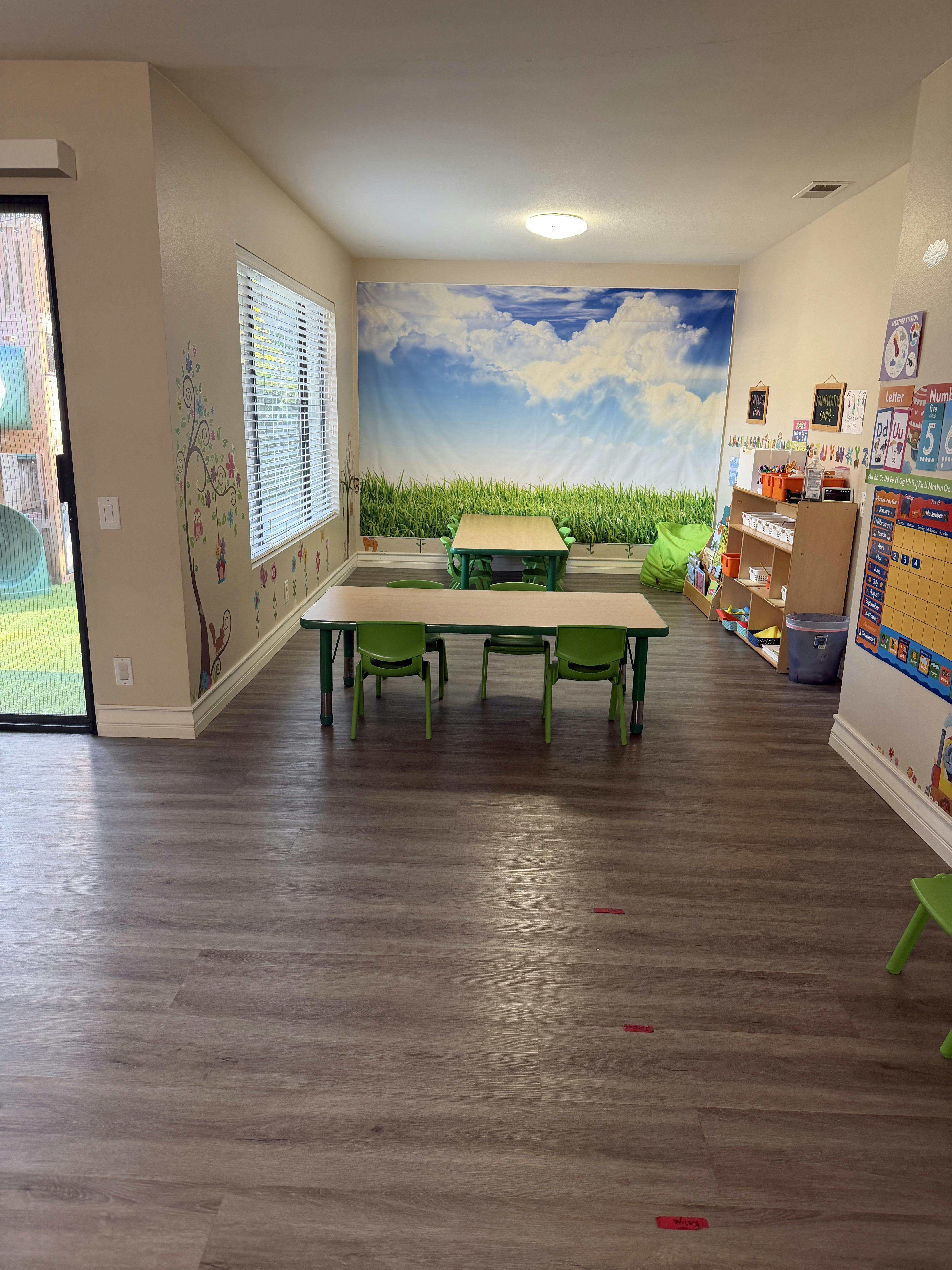 Classroom with small tables and chairs, sky and grass mural on wall