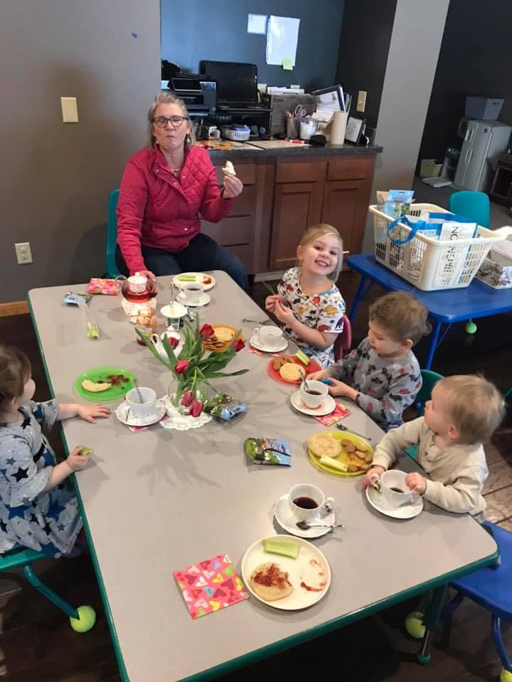 Adult and multiple children sitting around a table with teacups and snacks
