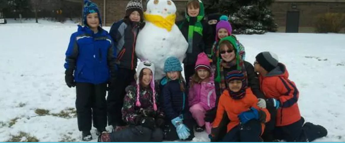 Group of children and adults posing with a snowman in the snow