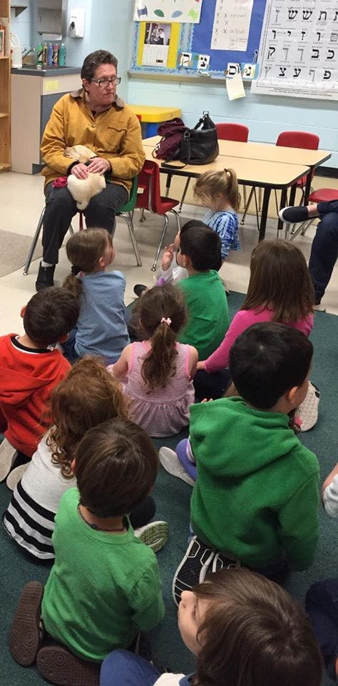 Person holding a small animal, surrounded by children sitting on the floor